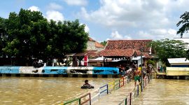 Warga Kelurahan Patemon, Kecamatan Kota Pamekasan bersiaga di dekat sungai dengan kondisi volume air penuh. (MOH. IQBALUL KHAVEI MZ / KLIKMADURA)