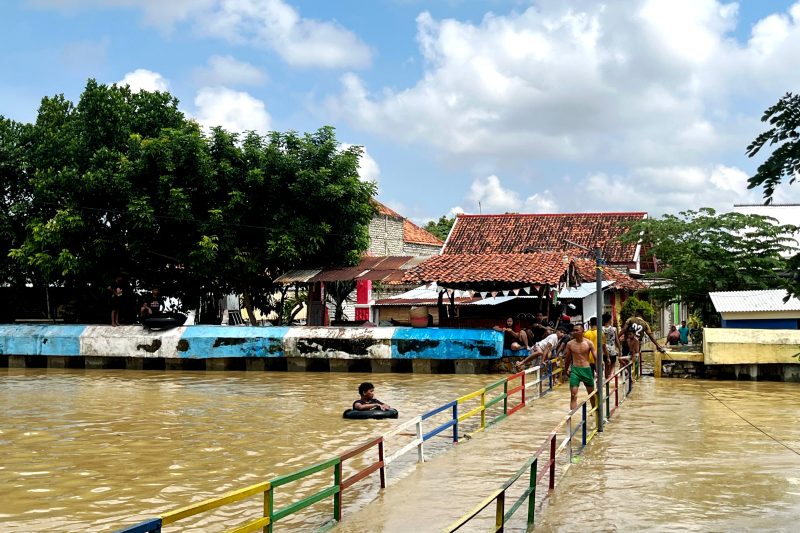 Warga Kelurahan Patemon, Kecamatan Kota Pamekasan bersiaga di dekat sungai dengan kondisi volume air penuh. (MOH. IQBALUL KHAVEI MZ / KLIKMADURA)