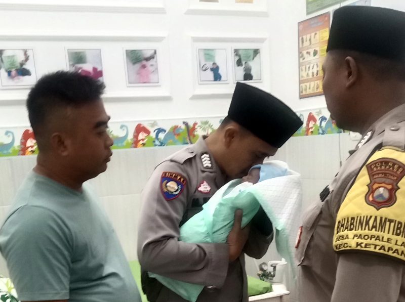 Bhabinkamtibmas Desa Ketapang Barat, Bripka Moh. Jufri mengazani bayi yang ditemukan di area persawahan Desa Ketapang Barat, Kecamatan Ketapang, Sampang. (ISTIMEWA)