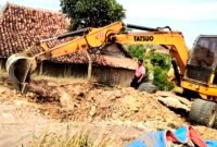 Warga Dusun Gunung, Desa Pasarenan, Kecamatan Kedungdung, Kabupaten Sampang berada di sekitar alat berat yang digunakan untuk memperbaiki jalan rusak dengan swadaya. (IBNU ANSORI / KLIKMADURA)