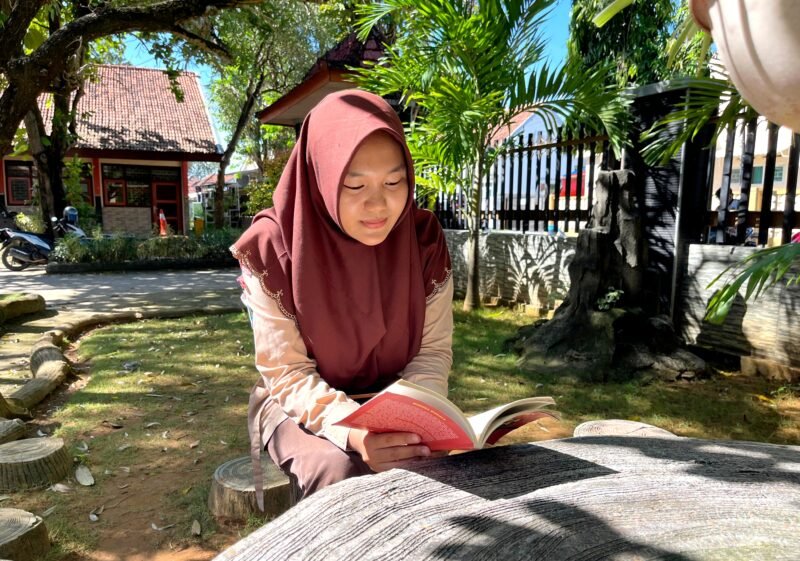Siswi SMAN 1 Pamekasan Sabrina Yasmin Firyal Siswanto sedang membaca buku di halaman sekolah (LAILIYATUN NURIYAH/KLIK MADURA).