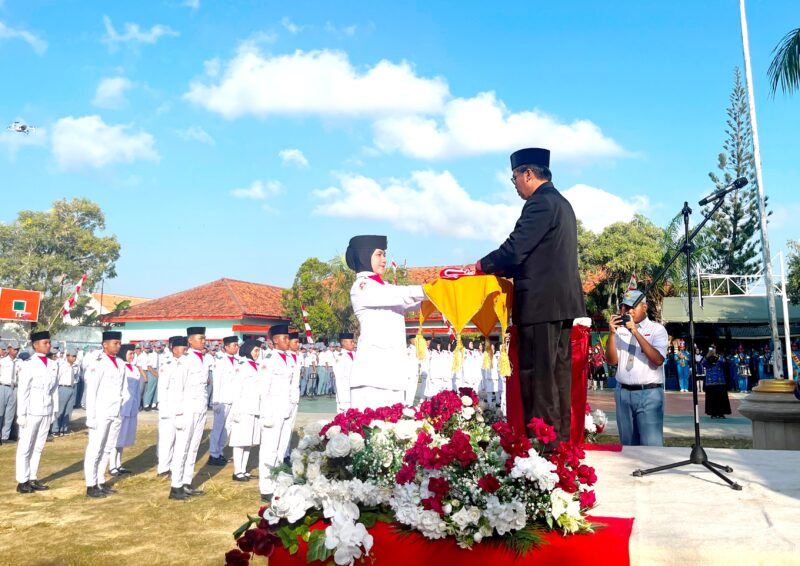 Kepala SMAN 2 Pamekasan Moh. Arifin menyerahkan bendera merah putih kepada pengibar bendera dalam rangka upacara memperingati HUT ke-81 Kemerdekaan Republik Indonesia. (LAILIYATUN NURIYAH / KLIKMADURA)